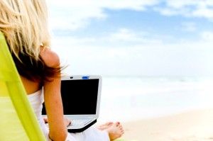 A young woman sitting on the beach with laptop computer